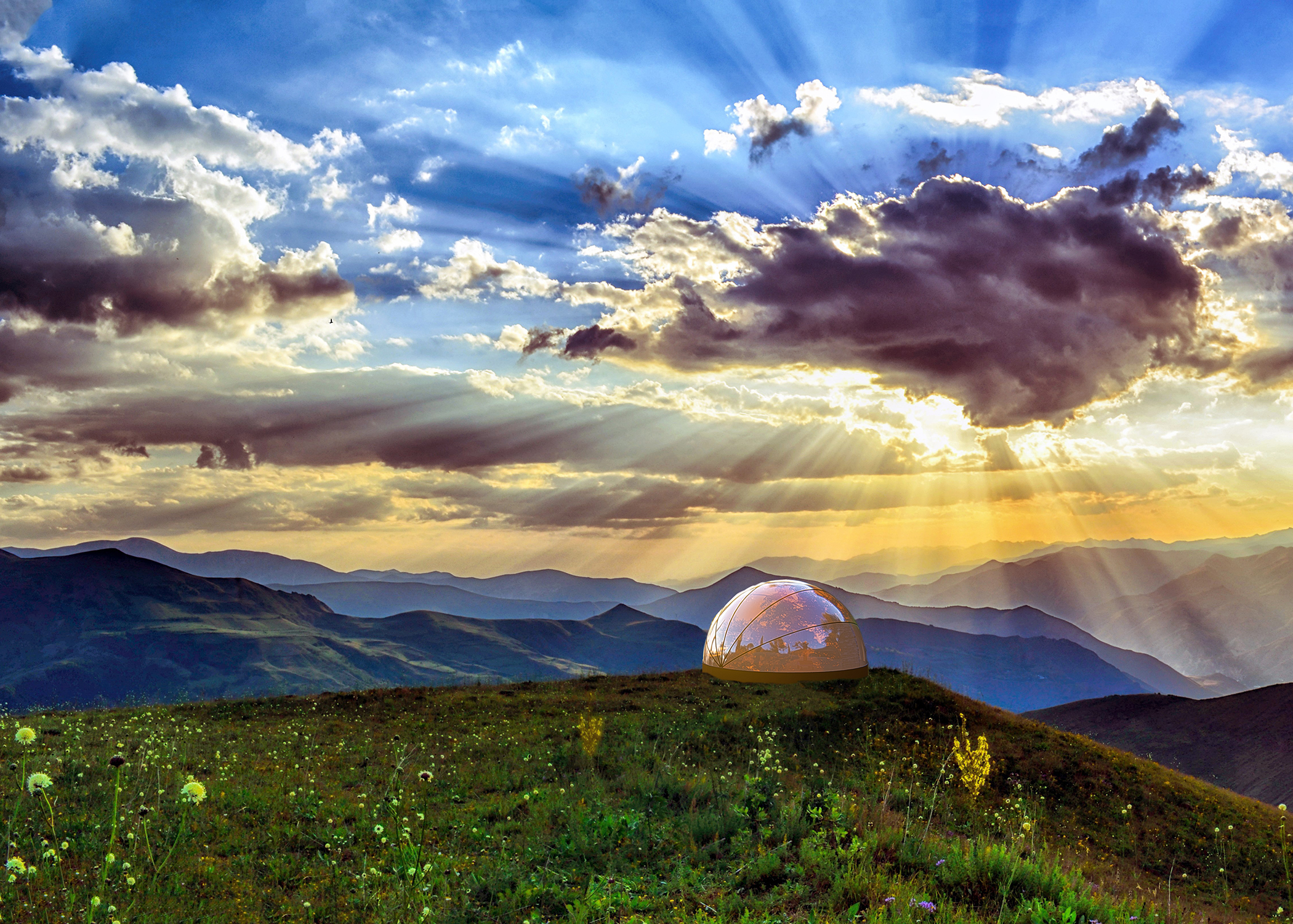 Bio dome on grassy hillside with mountains in background and sun shining through clouds