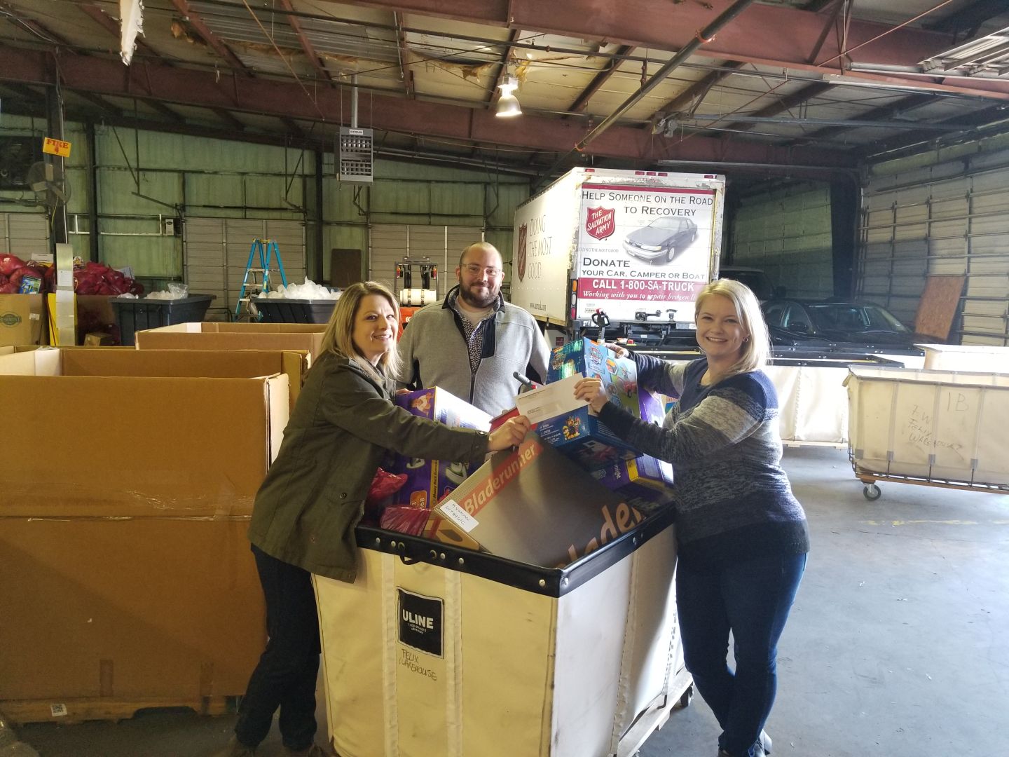 Three e4h employees next to cart filled with donations at Salvation Army warehouse