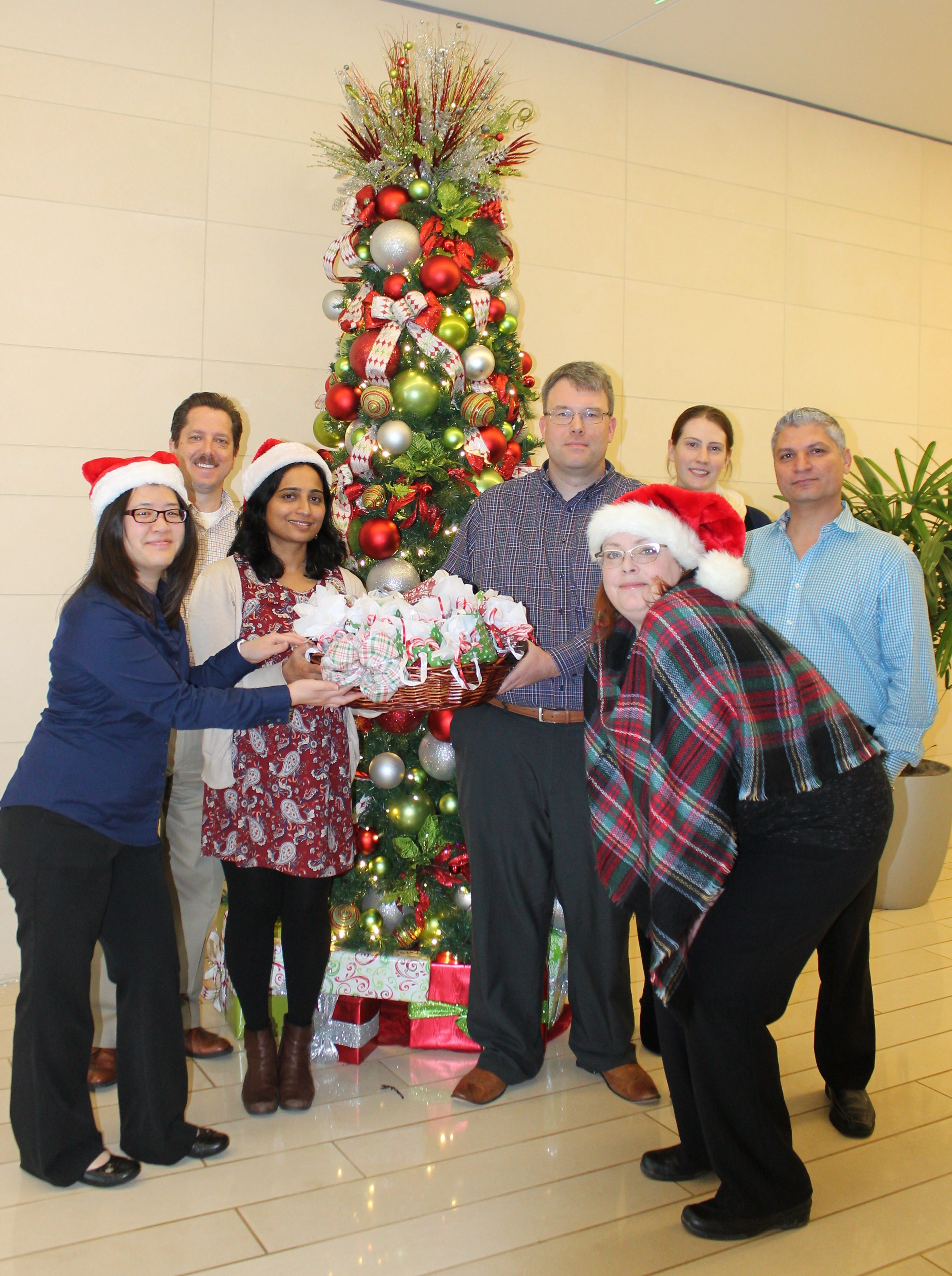 Group of seven people in front of Christmas tree holding basket of holiday treats