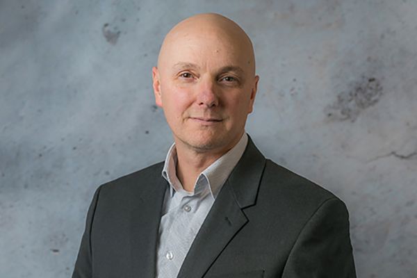 Man smiles while wearing a grey button-down shirt and black blazer - Thomas Morris