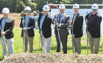 E4H team members wearing business suits with hardhats and shovels get ready to break ground on a medical center